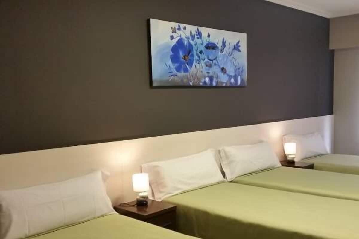 Una habitación de hotel con dos camas, cada una con una colcha verde y almohadas blancas. Hay un cuadro en la pared sobre las camas.