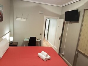 Ein Hotelzimmer mit einem roten Bett, einem Schreibtisch mit Stuhl, einem an der Wand befestigten Fernseher und einer Tür.