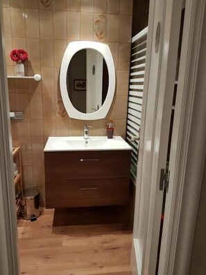 Ein Badezimmer mit einem Holzkosmetikschrank, einem runden Spiegel und einem weißen Waschbecken.