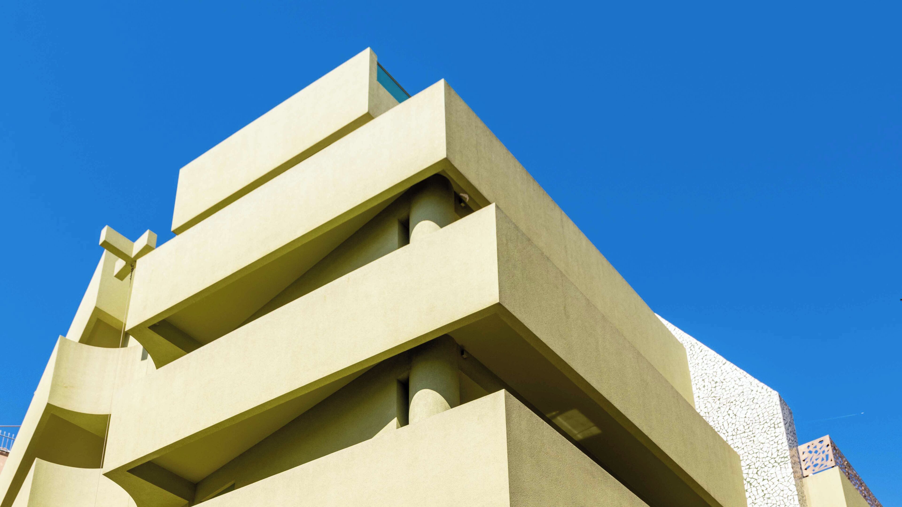 A modern building with a geometric design, featuring multiple balconies and a flat roof.