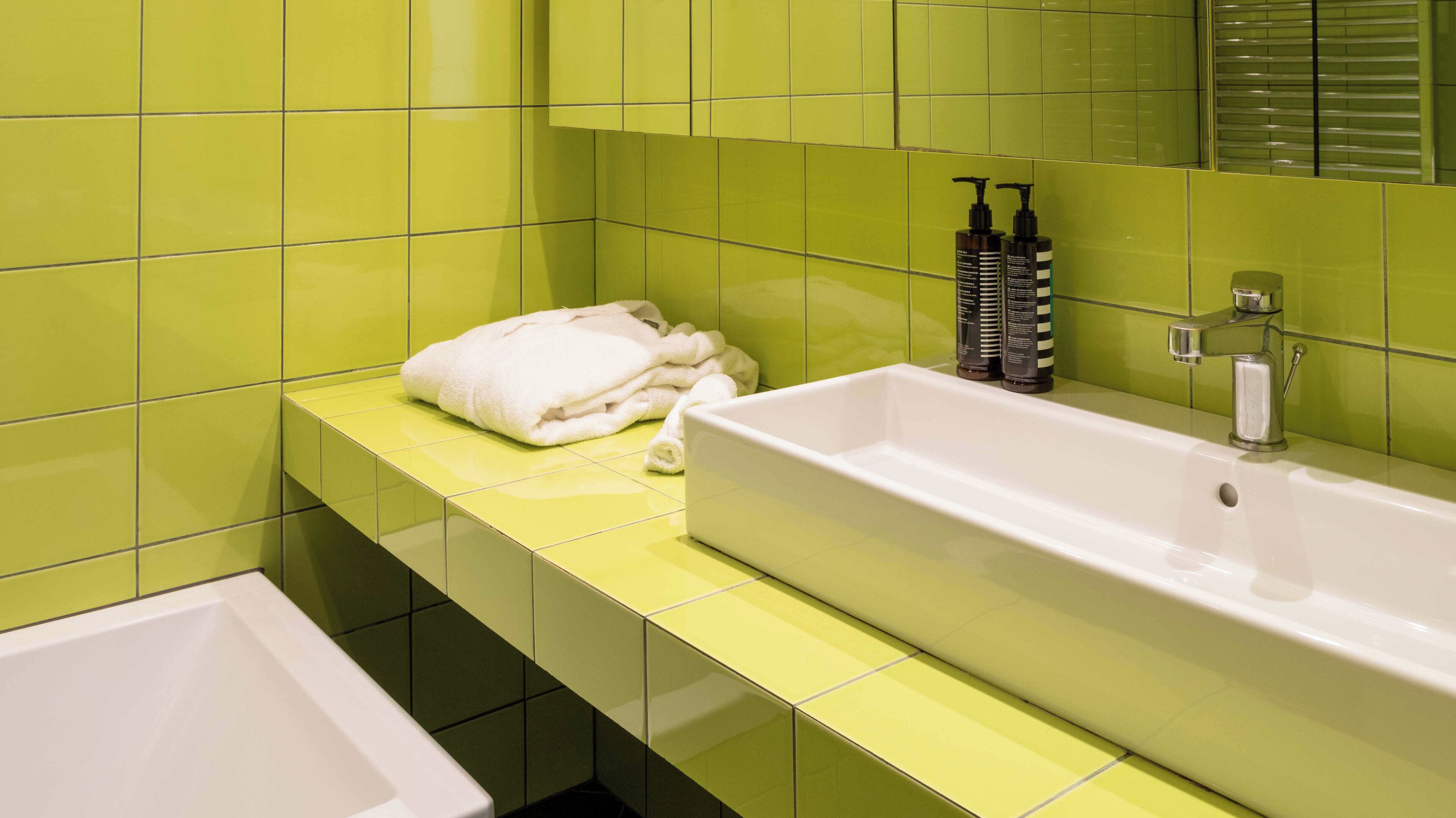 A bathroom with a white sink, green tiles, and a white bathtub.