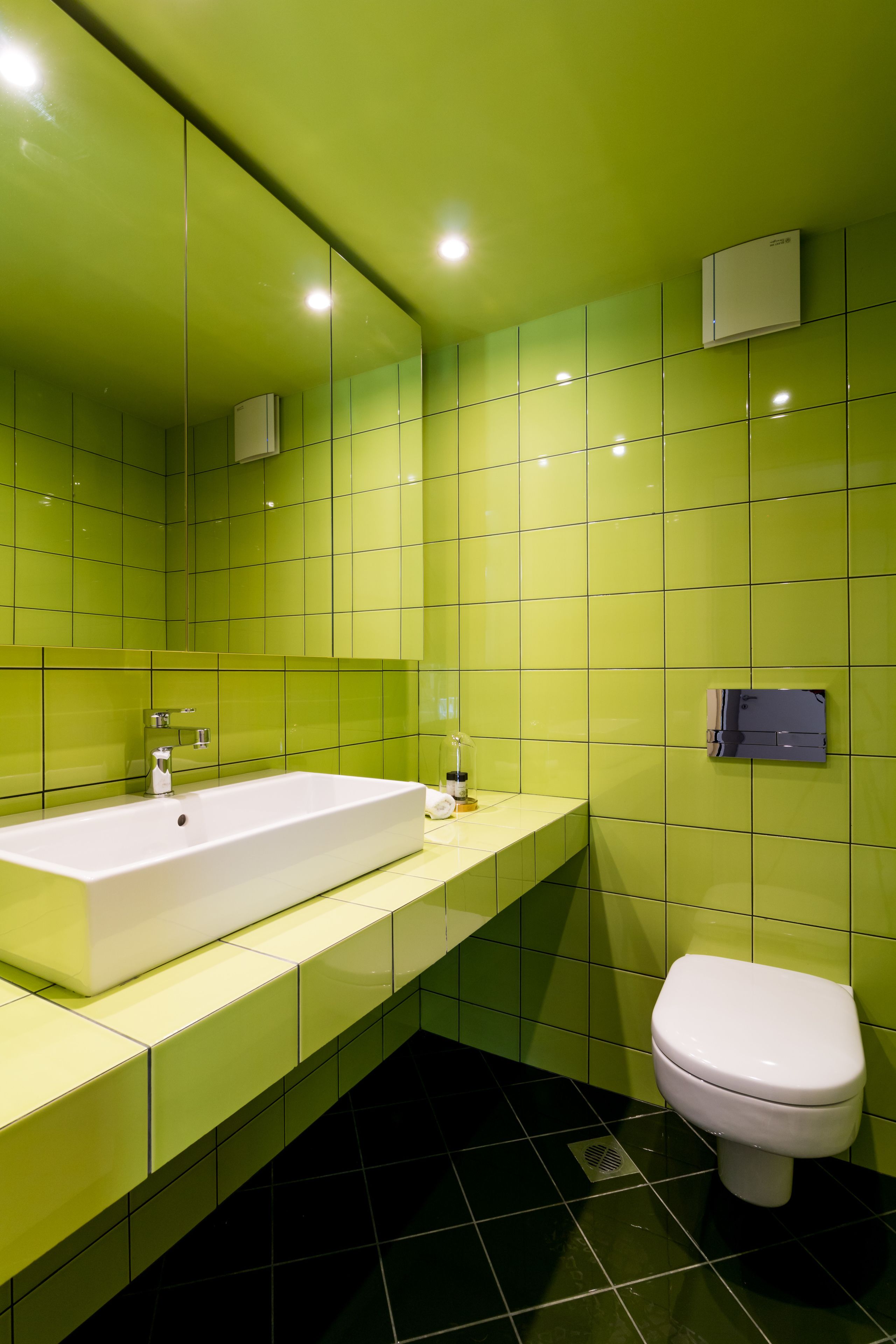 A bathroom with a large white bathtub, a white toilet, and green tiled walls.