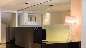 A modern reception area with a glass desk, a large mirror, and a decorative lamp. - Athens Mosaico Suites and Apartments (Athens)