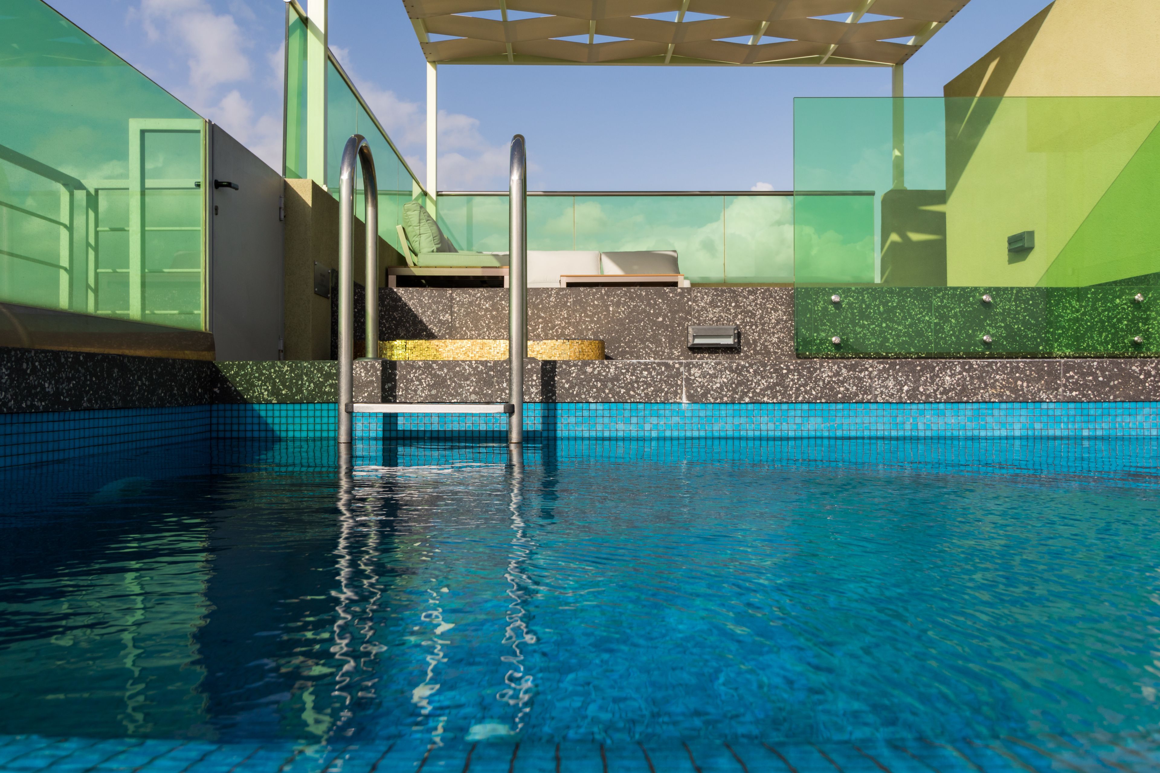 A swimming pool with clear blue water, a metal ladder, and a green and white tiled wall.
