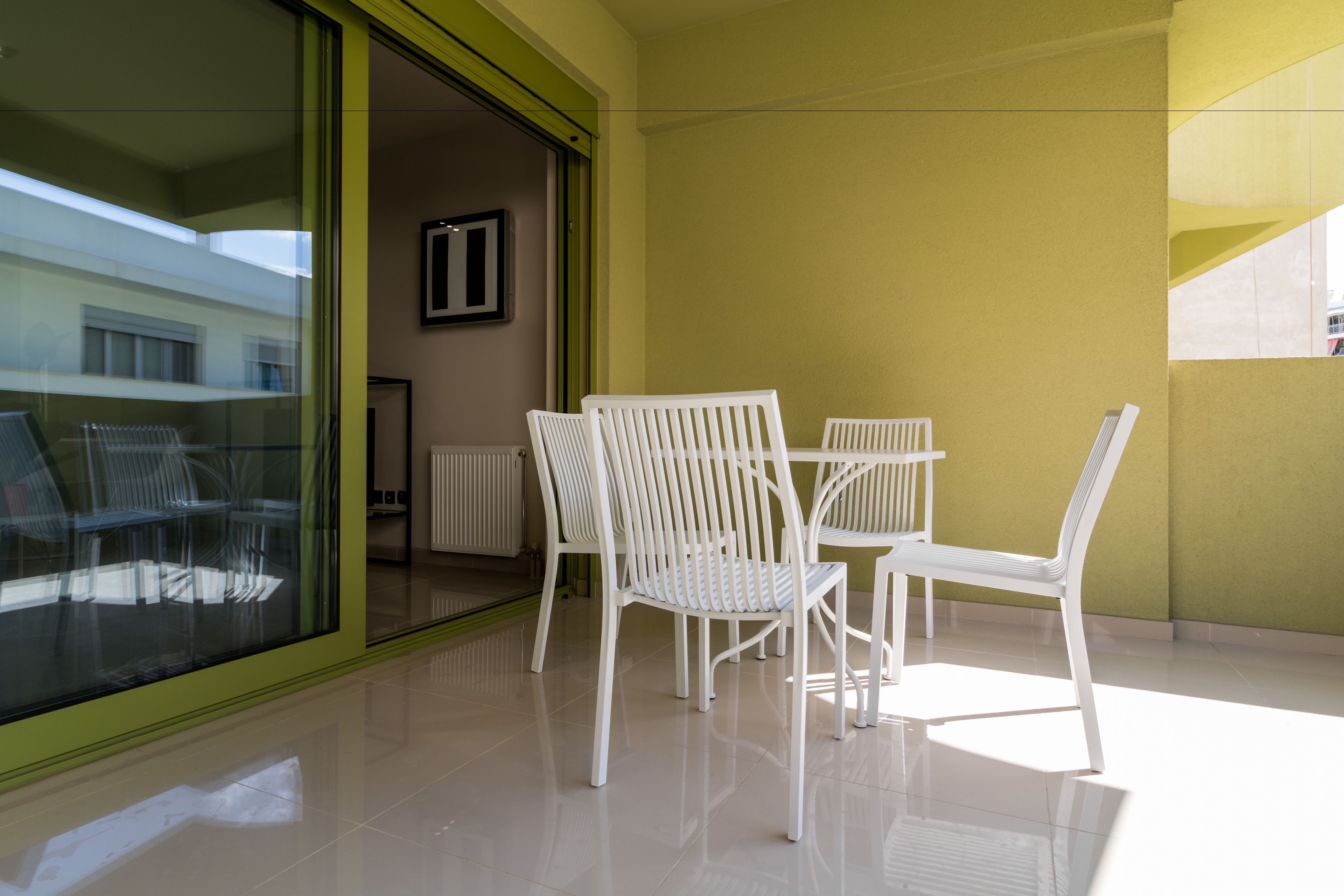 Uma varanda com cadeiras e mesa brancas, uma porta de vidro e uma parede amarela.