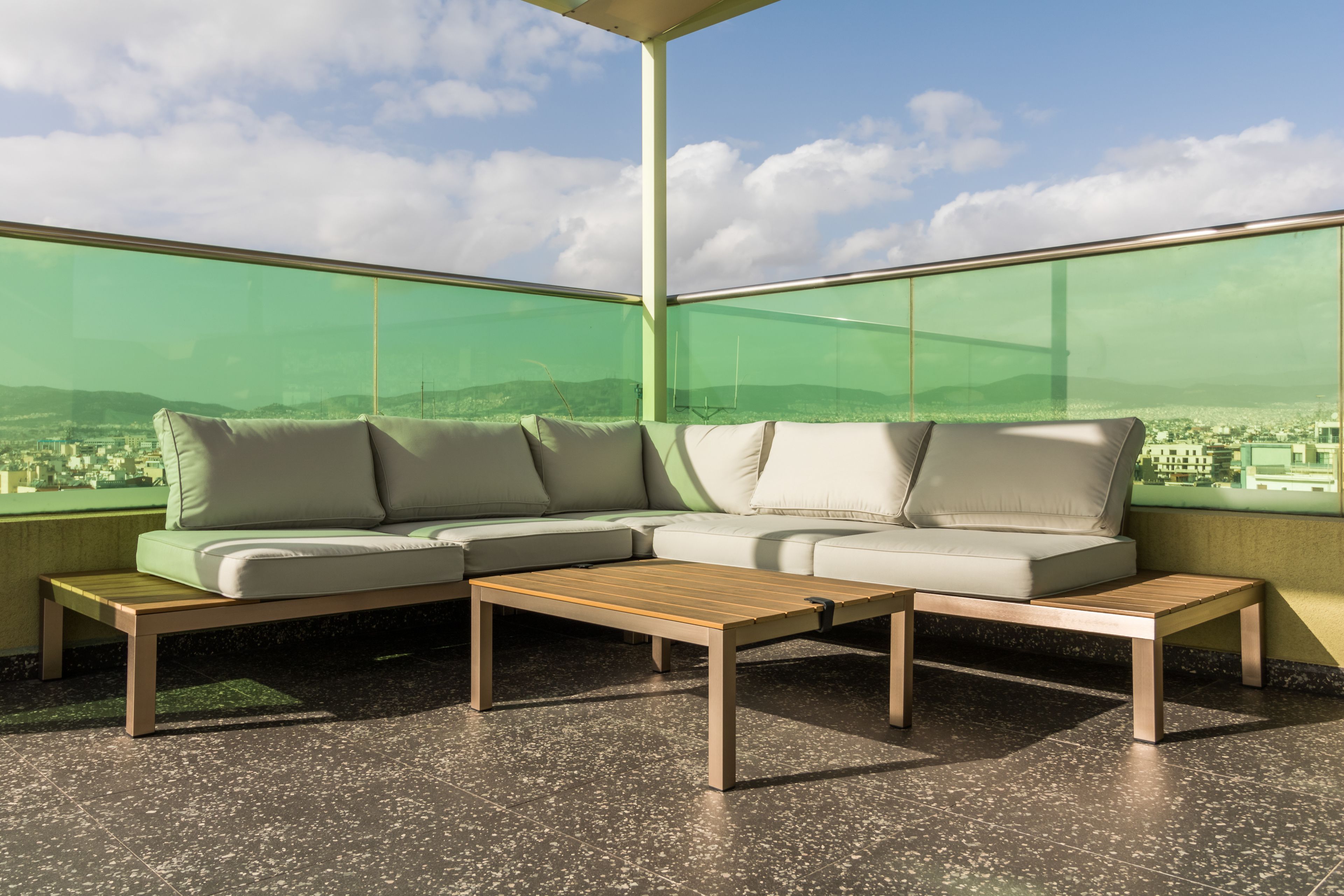 Un balcon moderne avec une cloison en verre teinté, un canapé d’angle beige et une table basse en bois.