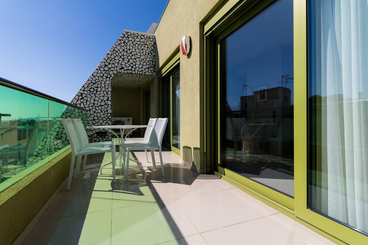 A balcony with a glass railing, a table, and two chairs.