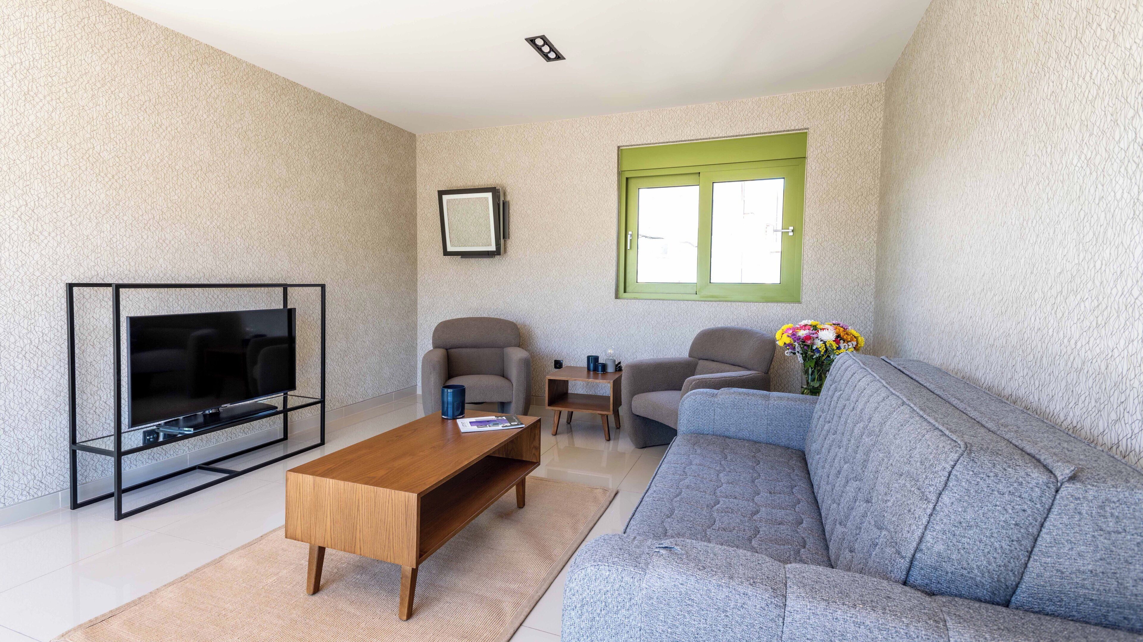 A modern living room with a flat-screen TV, a wooden coffee table, two armchairs, a sofa, and a small side table.