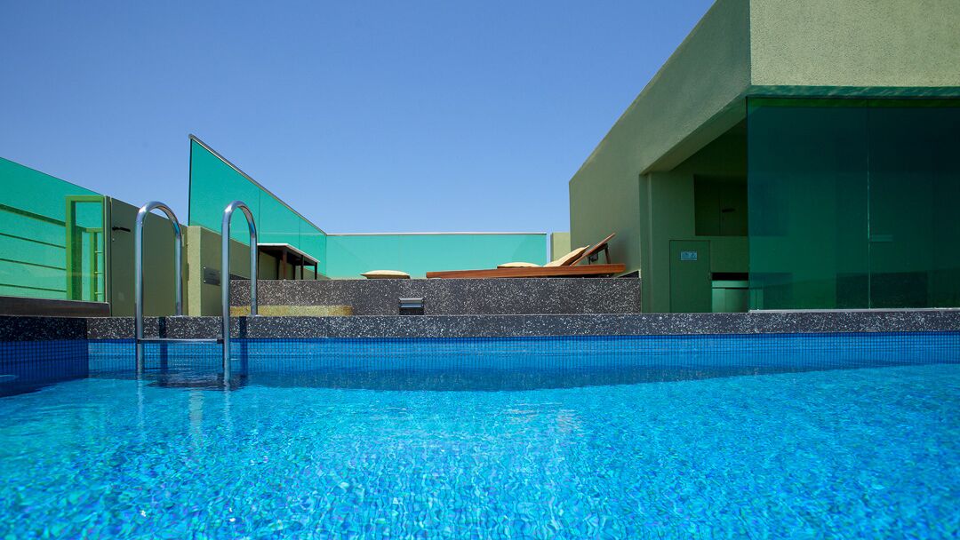 Piscina com superfície de água azul cristalina, rodeada por um muro de pedra baixo e grades de metal.