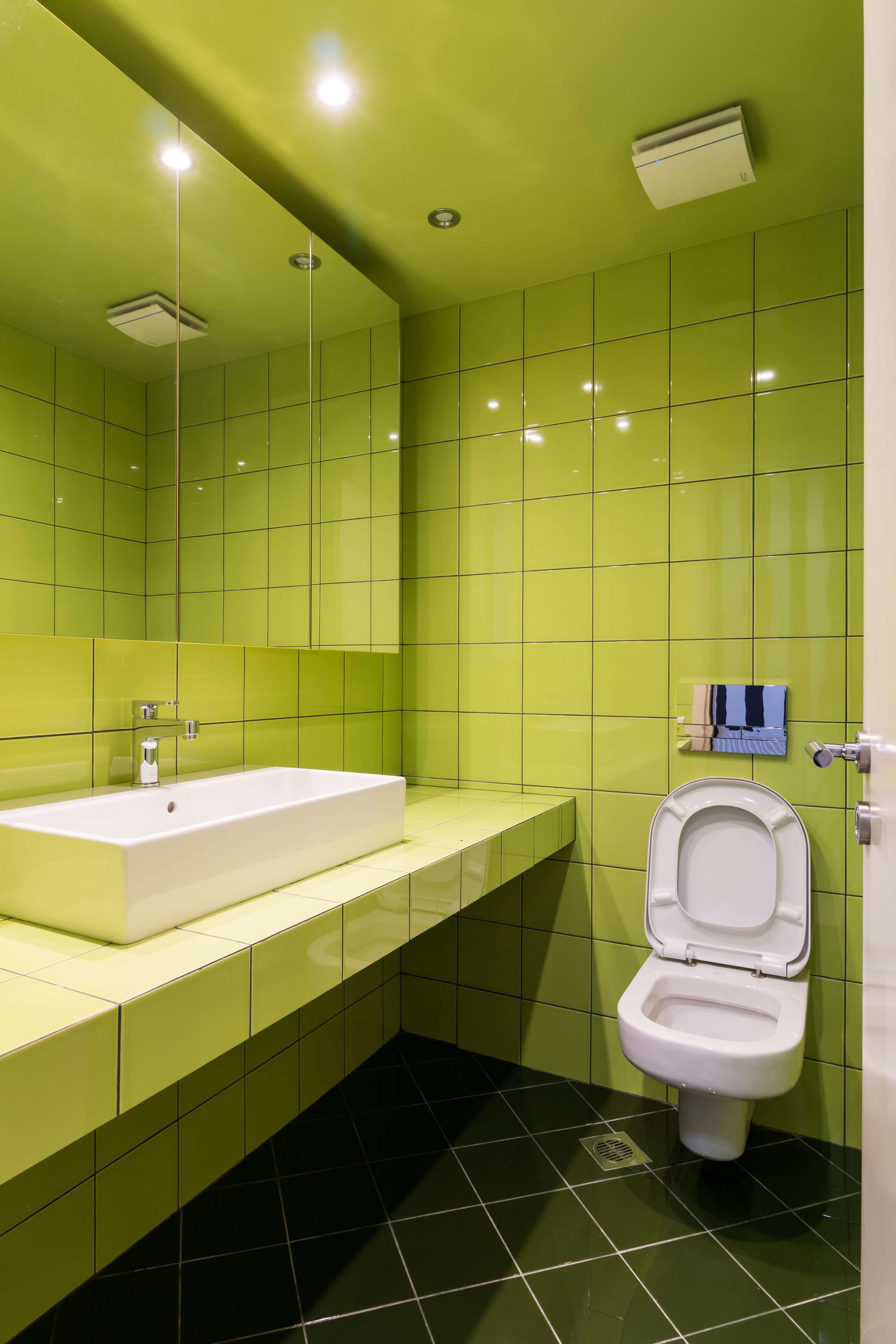 Une salle de bain avec des murs recouverts de carreaux verts, un lavabo blanc et des toilettes.