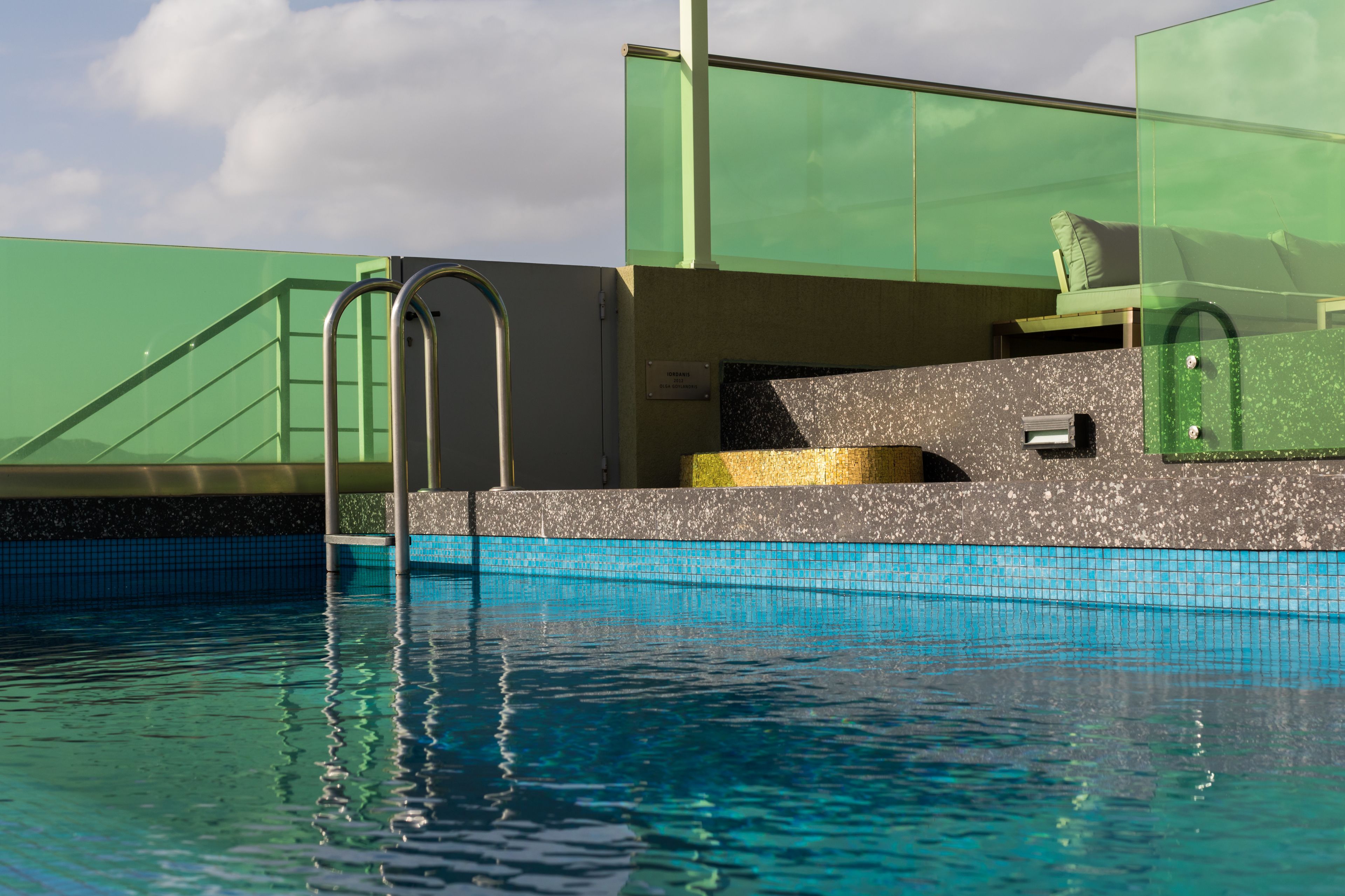 Une piscine dotée d’une terrasse fermée par des parois en verre, d’un petit espace salon et d’une échelle en métal.
