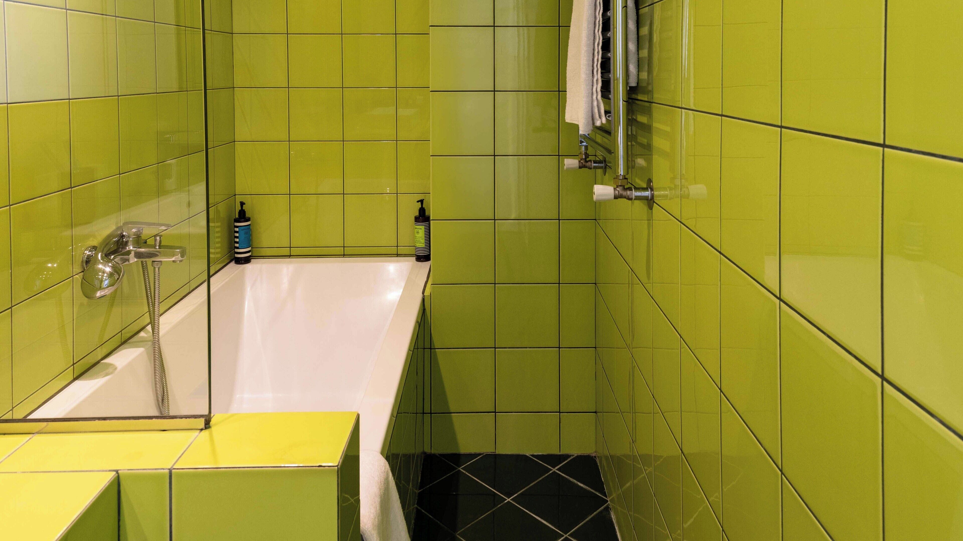 A bathroom with green tiles, a white bathtub, and a yellow sink.