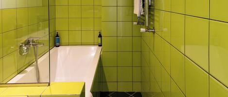 A bathroom with green tiles, a white bathtub, and a yellow sink.