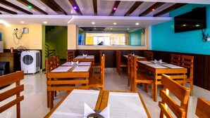 Un restaurante con mesas y sillas de madera, una barra con una persona detrás y un televisor colgado en la pared.