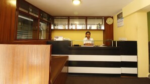 Zona de recepción con recepcionista, un reloj y un tablón de anuncios.