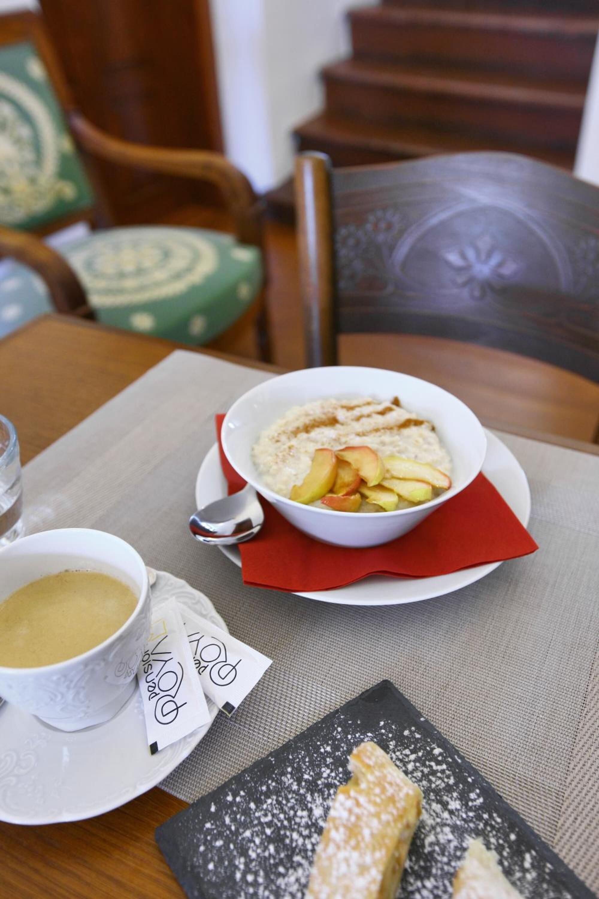 A breakfast setting with a bowl of oatmeal topped with fruit, a cup of coffee, and a pastry on a table.