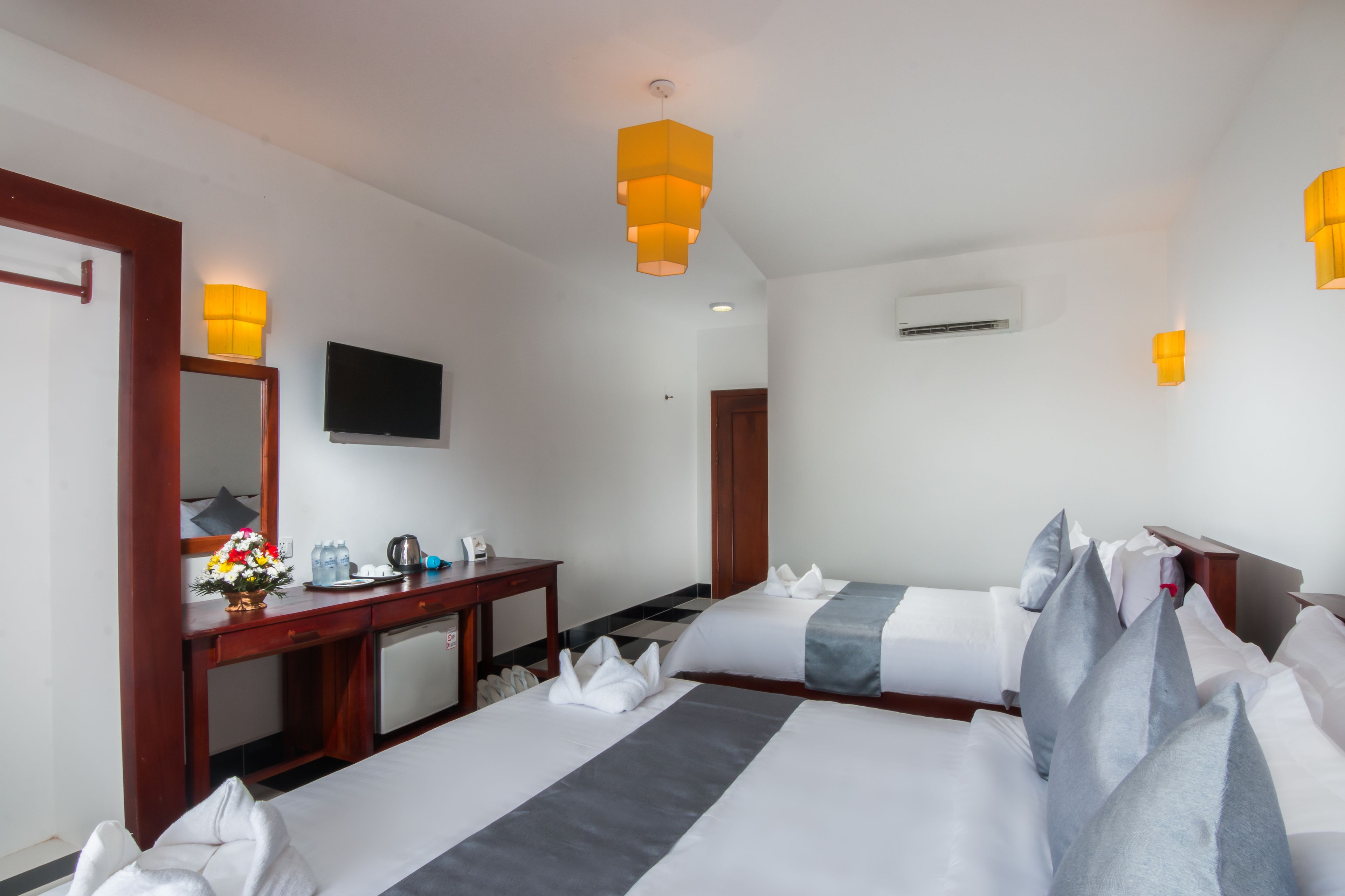 A hotel room with two beds, a desk, a TV, and a bathroom.