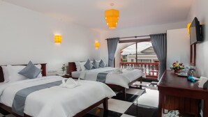 A hotel room with two beds, a desk, a chair, a small table with a vase of flowers, and a balcony with a view. - Bou Savy Villa (Siem Reap)