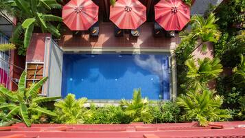 A pool area with three red umbrellas, surrounded by lush greenery and a tiled pool.