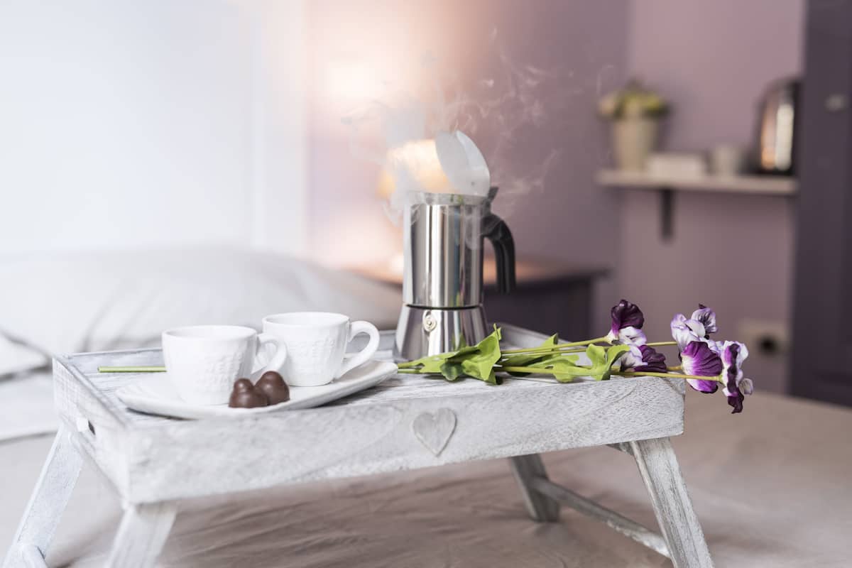 A breakfast setup with a coffee pot, two cups, and a tray with flowers and chocolates.