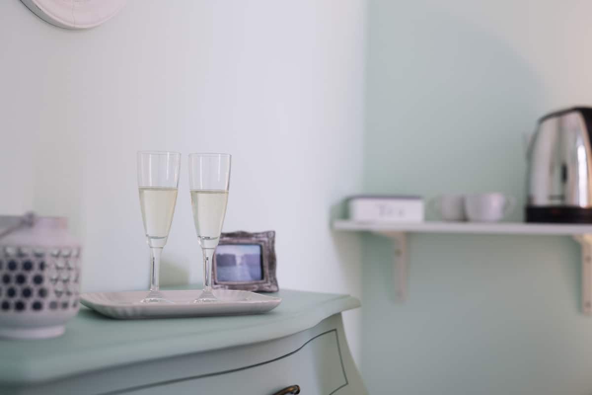 A teal dresser with two glasses of a clear liquid, a small framed photo, and a kettle on a shelf.