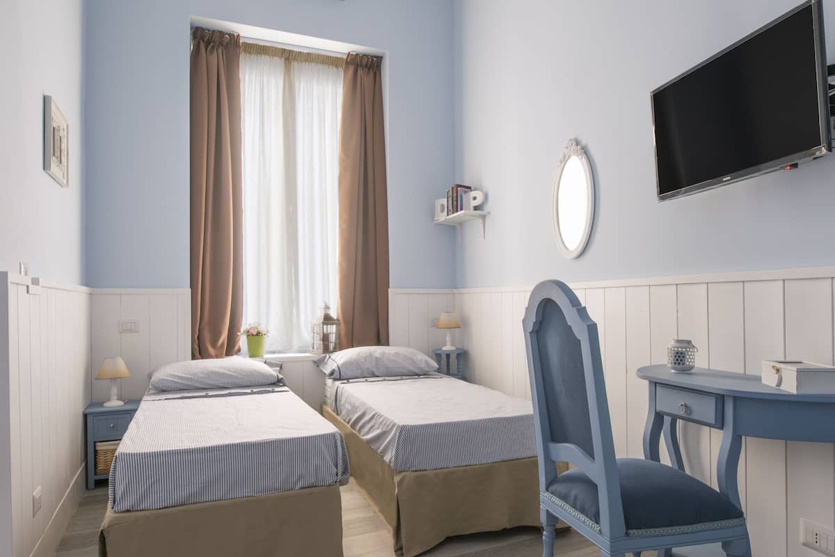 A bedroom with two beds, a desk, a chair, a TV, and a window with curtains.