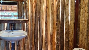 Maalaishenkinen kylpyhuone, jossa on puulankkuverhoiltu seinä, valkoinen pesuallas ja wc-istuin.