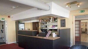 Un área de recepción con mostrador, estantes con botellas y copas, y un cartel que indica una salida.