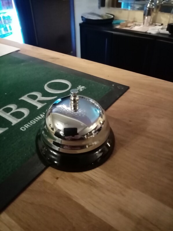 A hotel room with a wooden table, a green brochure, and a silver bell on the table.