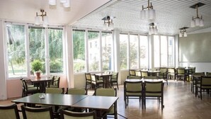Un comedor amplio con varias mesas y sillas, ventanas grandes que ofrecen vistas a zonas verdes, y un techo con lámparas colgantes.