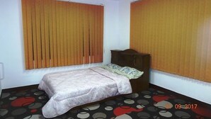A bedroom with a bed, a wooden headboard, and a window with blinds.