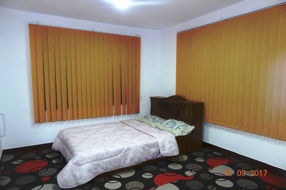 Un dormitorio con cama, cabecera de madera y ventana con persianas.