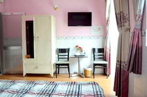 A bedroom with a bed, a wardrobe, two chairs, a small table with a vase, and a television on the wall.