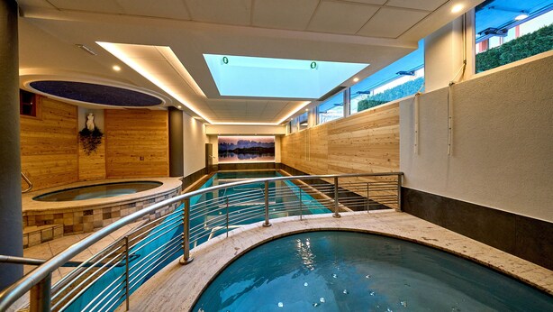 An indoor swimming pool with a skylight, wooden walls, and a view of the outside. - Hotel Cristina (Pinzolo)