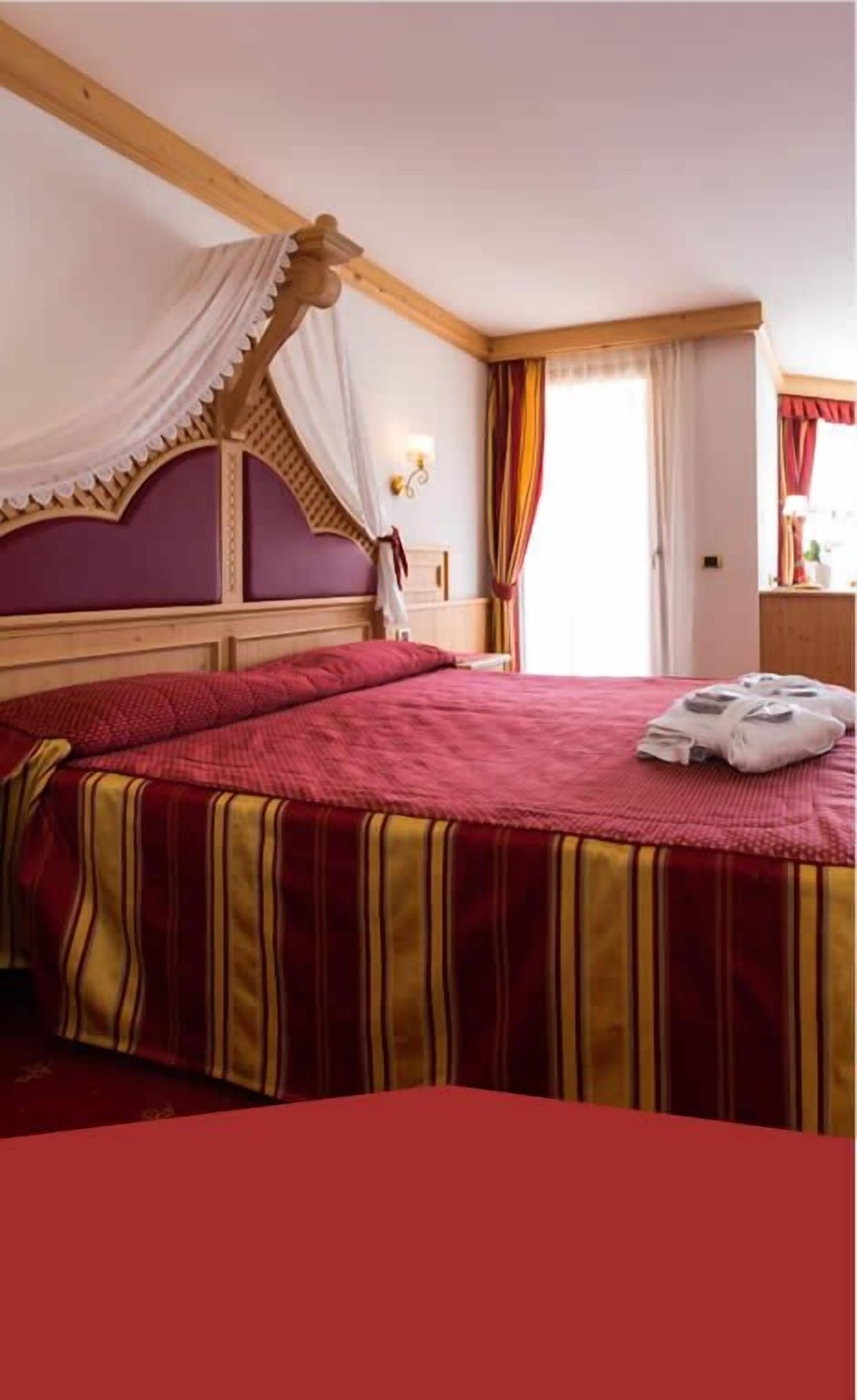 A room with a large bed, a canopy bed, and a window with curtains.