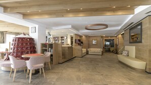 A spacious lobby with a wooden ceiling, a round table with chairs, a red spherical object, and a reception desk. - Hotel Cristina (Pinzolo)