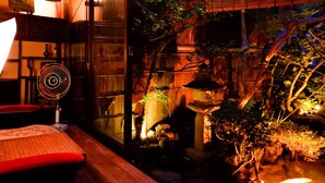 Una habitación tenuemente iluminada con una mesa de madera, una silla roja y un ventilador.