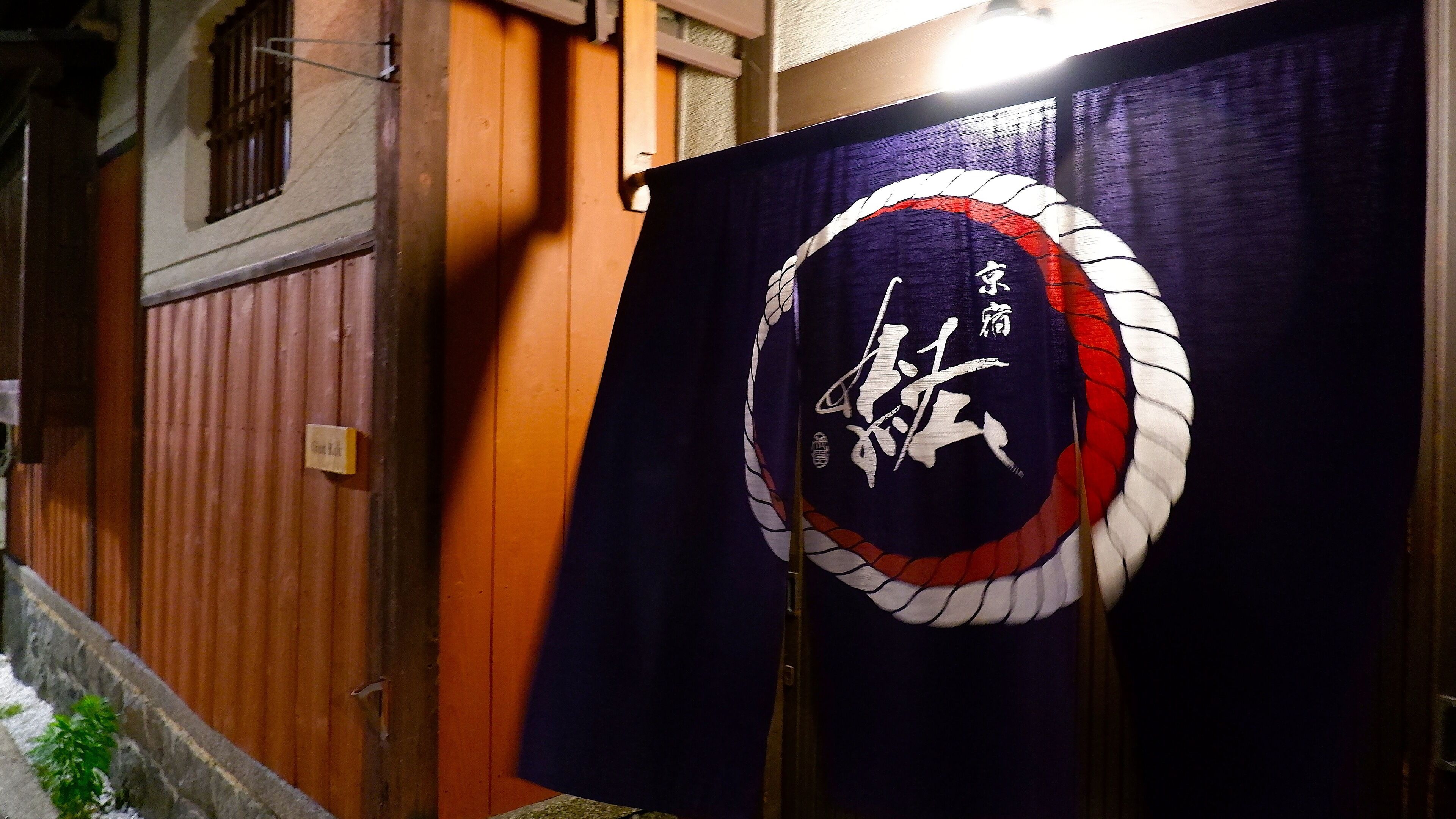 A traditional Japanese building with a wooden exterior and a dark blue banner featuring white calligraphy and a red and white design.