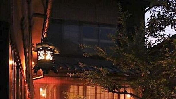Un jardín japonés tradicional con un farol de piedra, un estanque pequeño y una mesa roja.