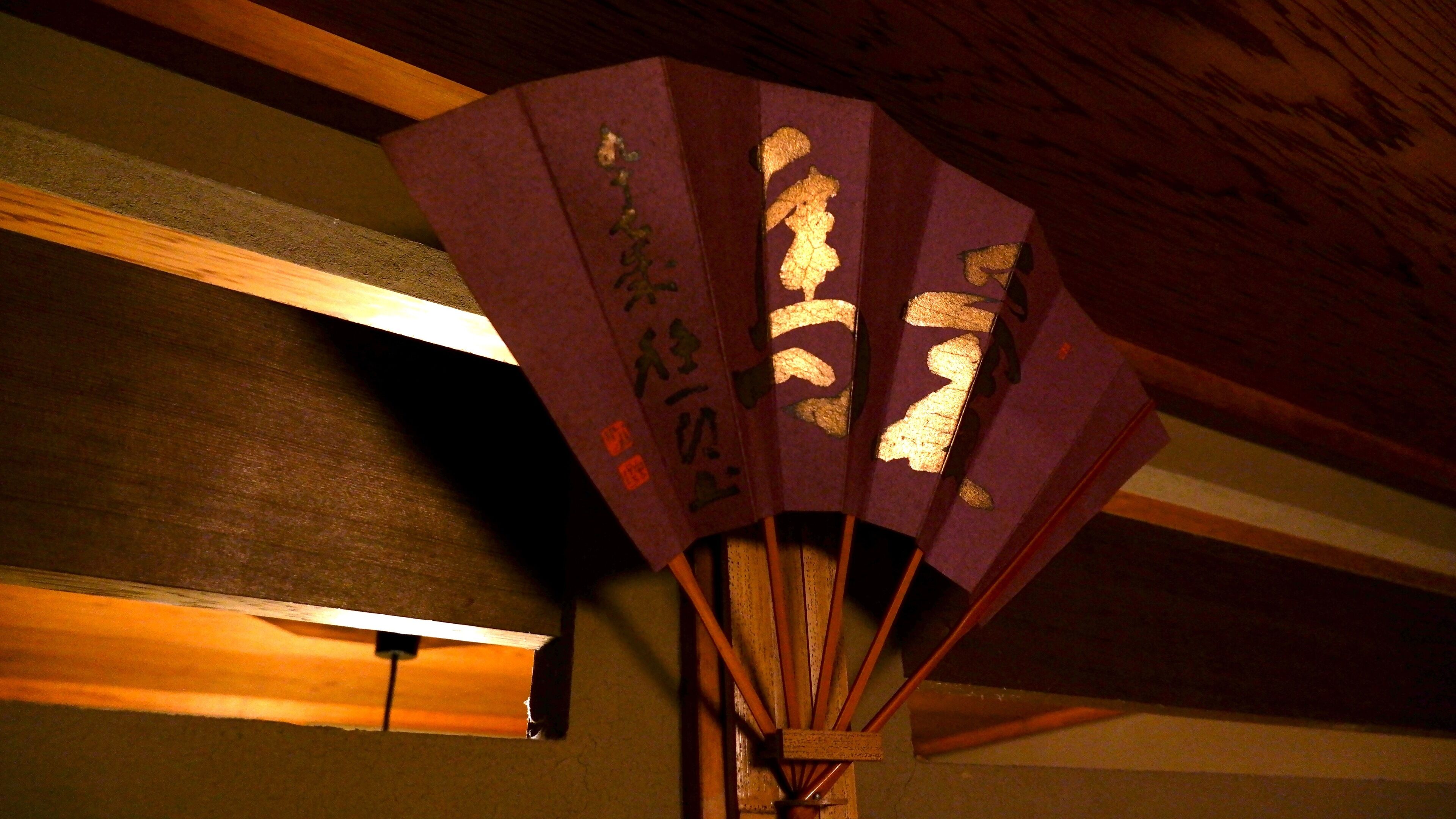 A traditional Japanese folding fan with calligraphy, wooden beams, and a light fixture.