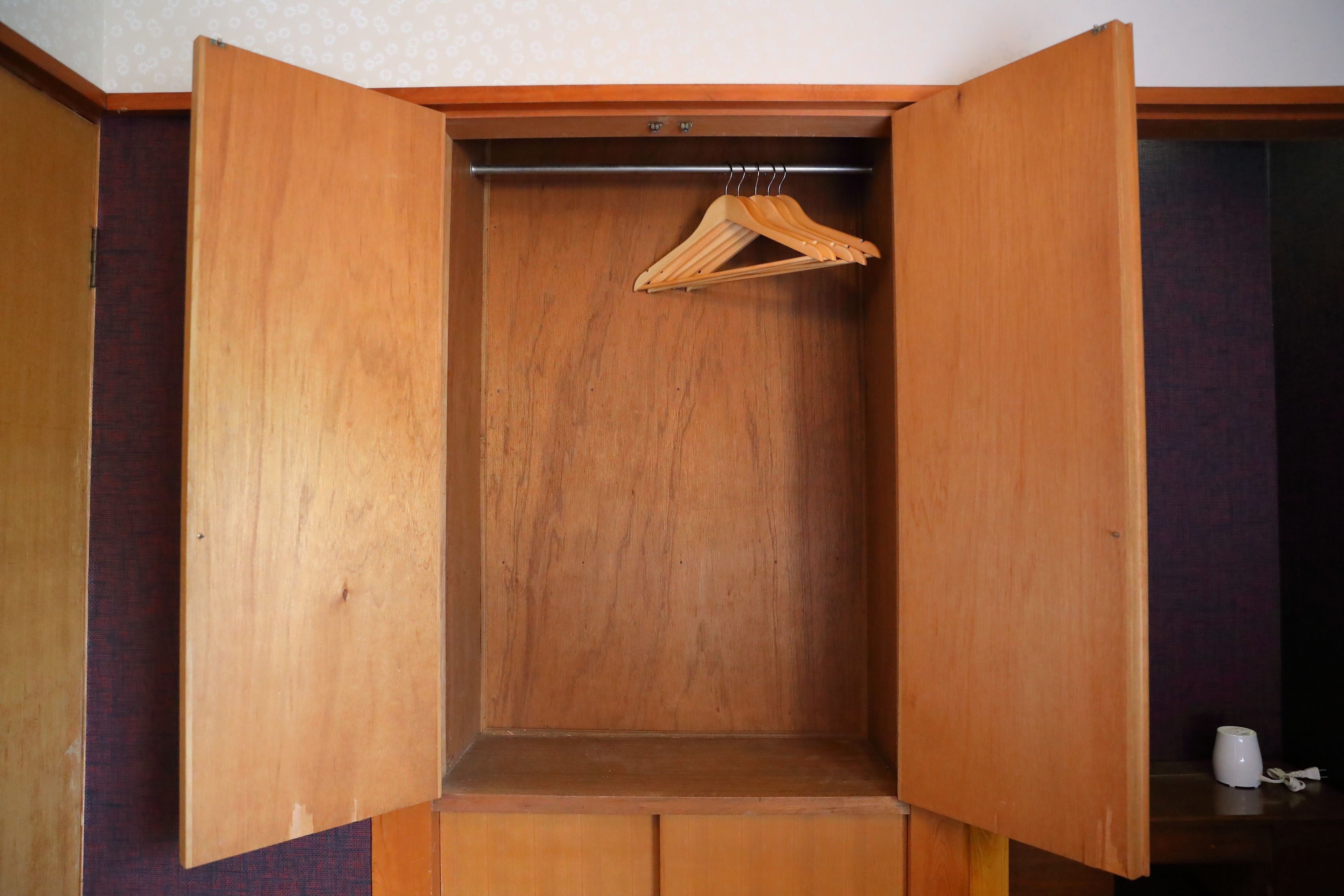 A wooden wardrobe with a hanging rod and a small shelf.