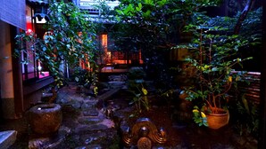 Un jardín japonés tradicional con faroles de piedra, un pequeño elemento acuático y abundante vegetación.