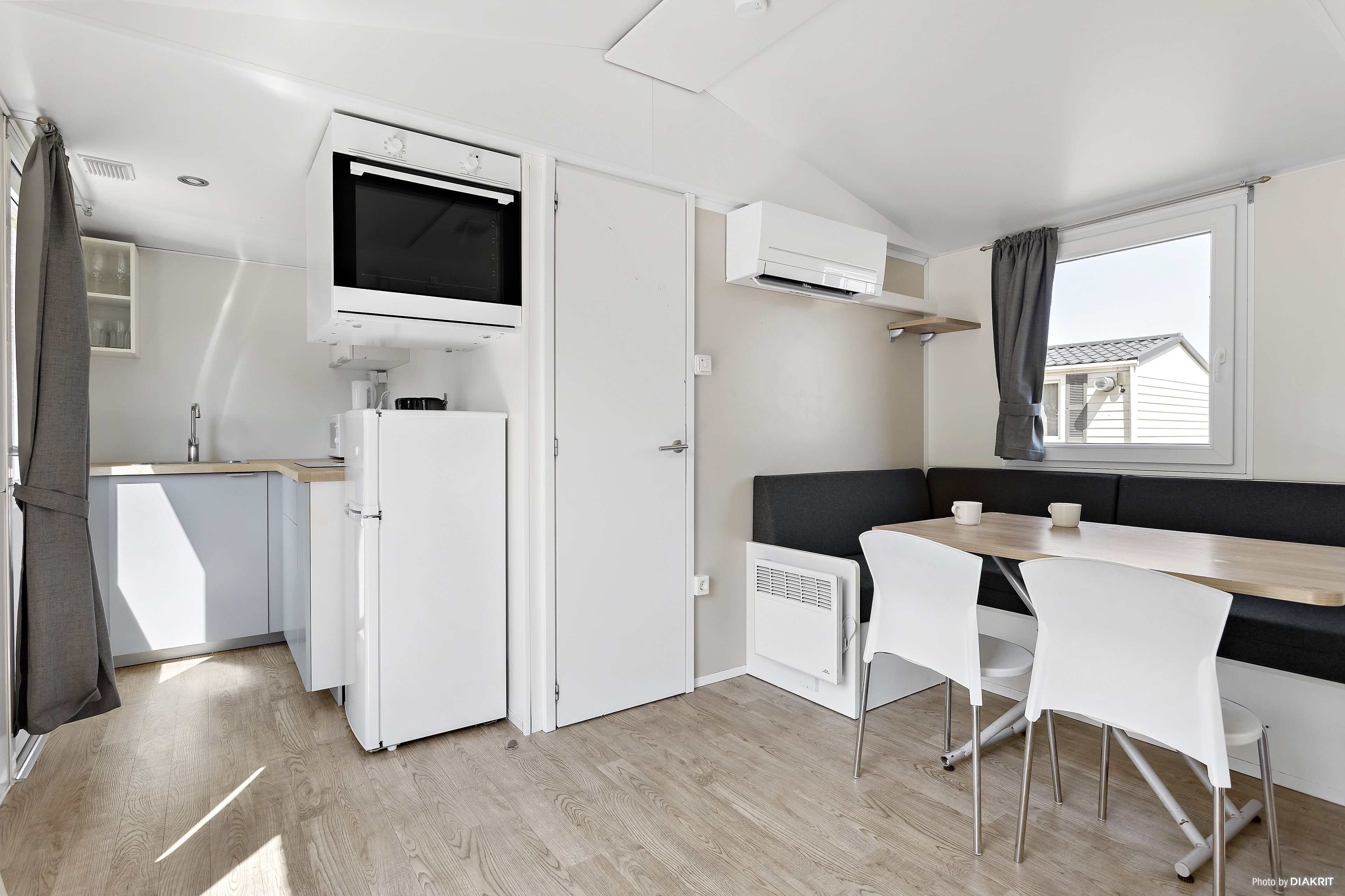 A compact kitchen with a built-in microwave, a refrigerator, and a dining area with a bench and chairs.
