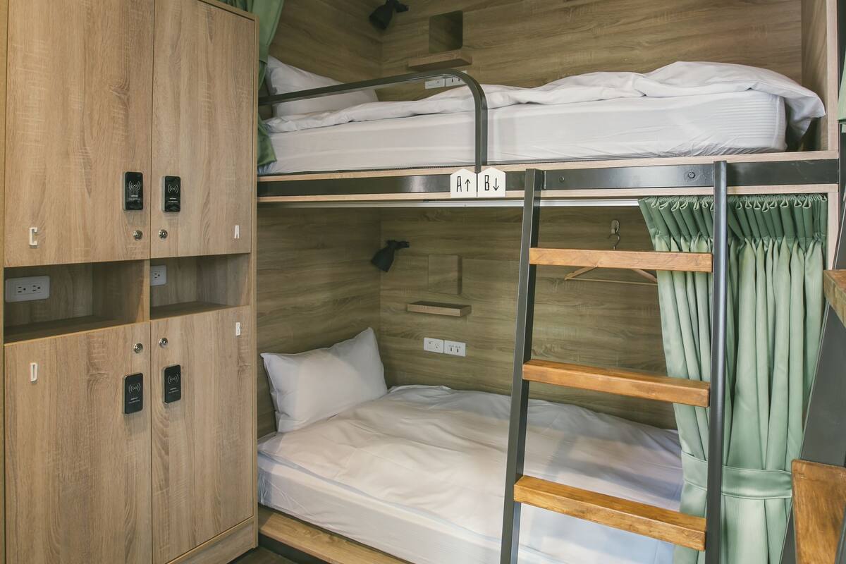 A bunk bed room with a wooden wardrobe, a ladder, and a hanging rack.