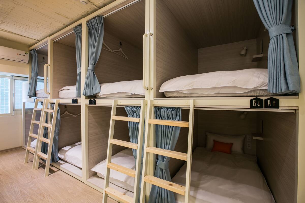 A bunk bed room with wooden frames, curtains, and a ladder.