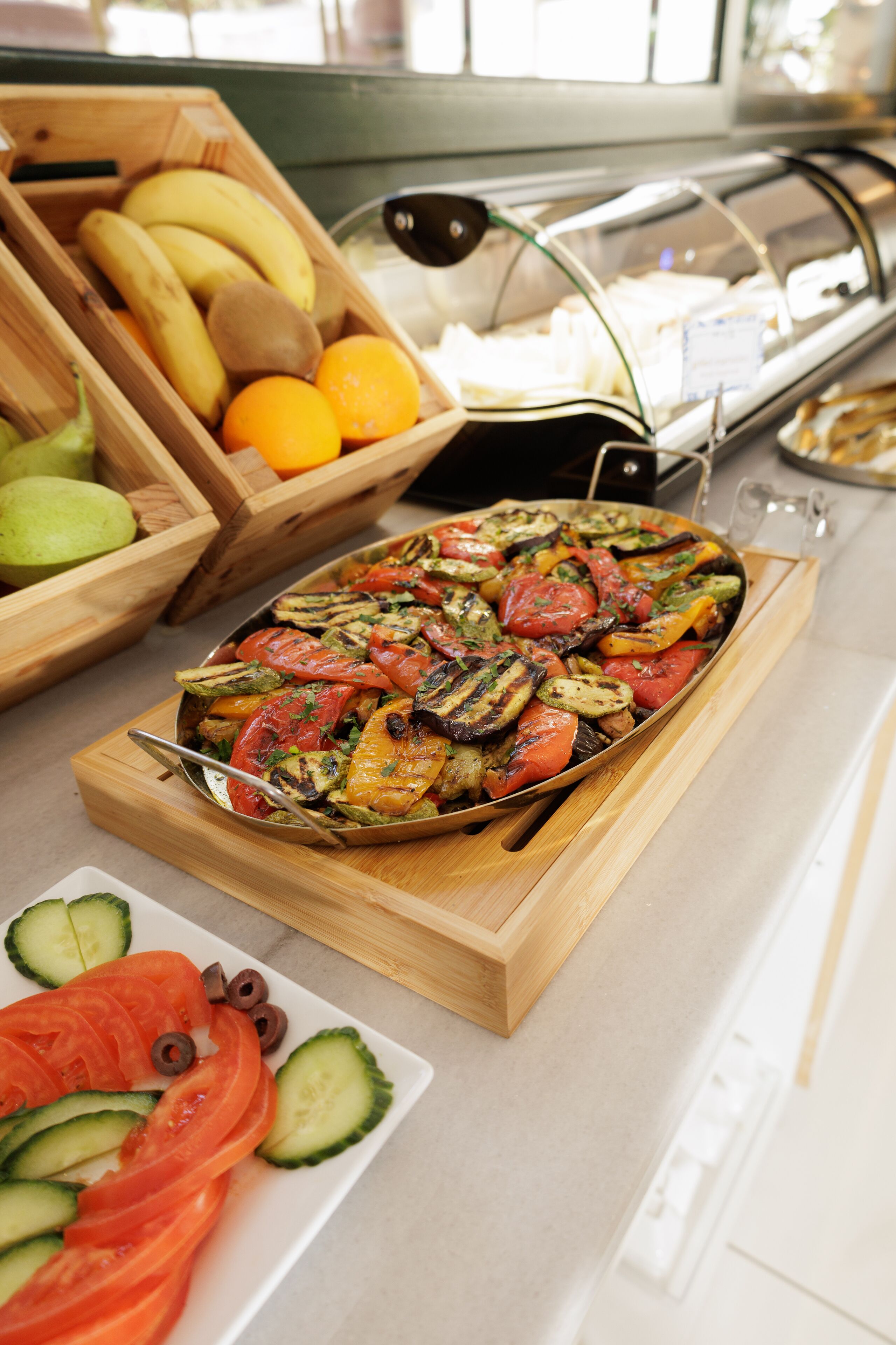 A buffet with a variety of fruits and vegetables, including sliced tomatoes, cucumbers, and bananas.