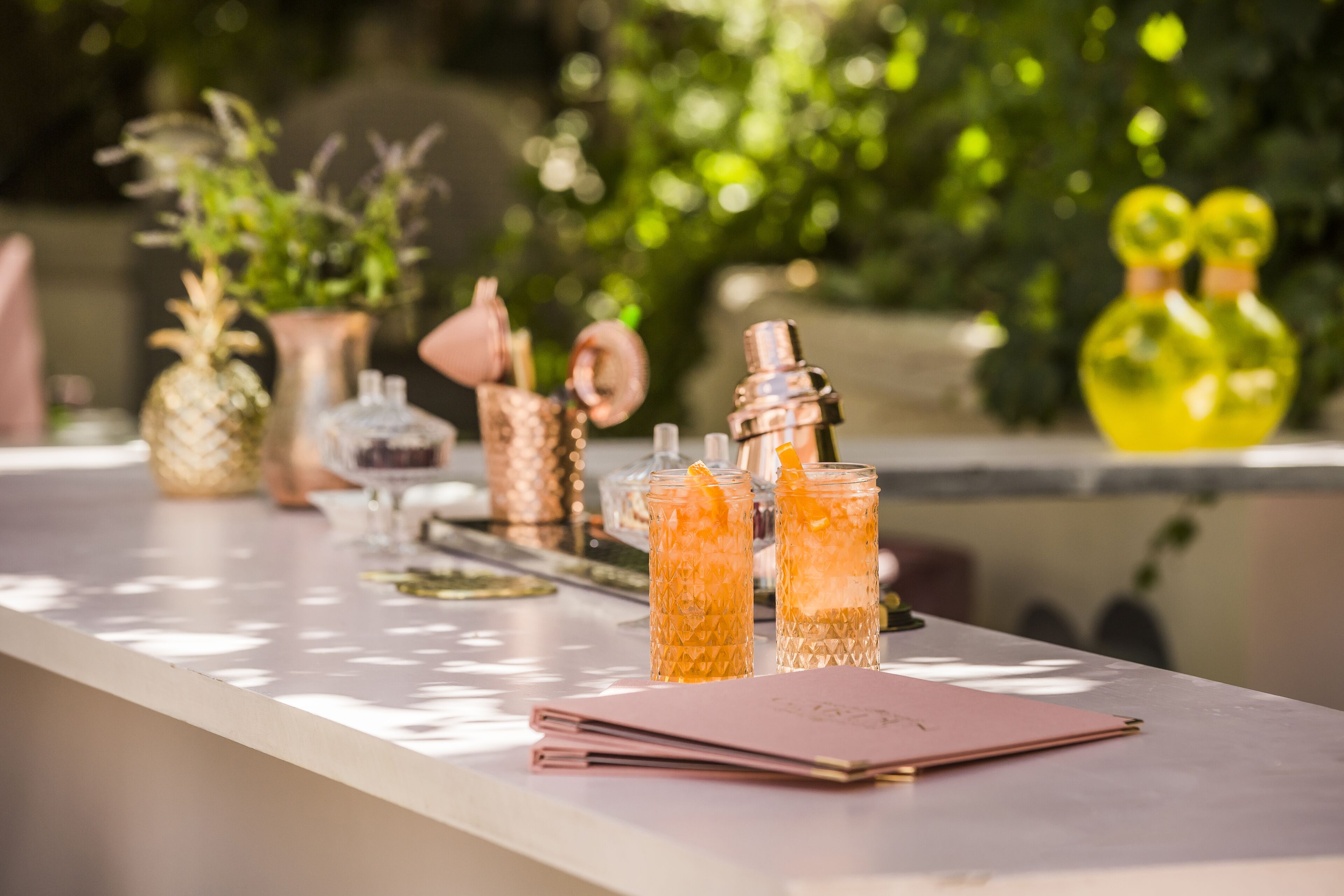A bar area with a long counter, several glasses of beverages, and decorative items like vases and a pineapple.