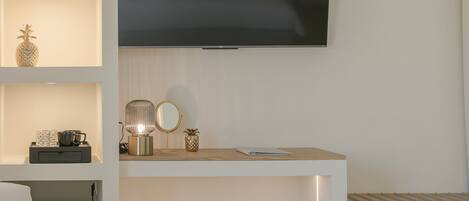 A modern living room with a flat-screen TV mounted on the wall, a white sofa, a small round stool, and shelves with decorative items.