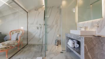Een moderne badkamer met een glazen douchecabine, marmeren vloer, een wastafelmeubel met een wastafel en een stoel met een bloemenprint.