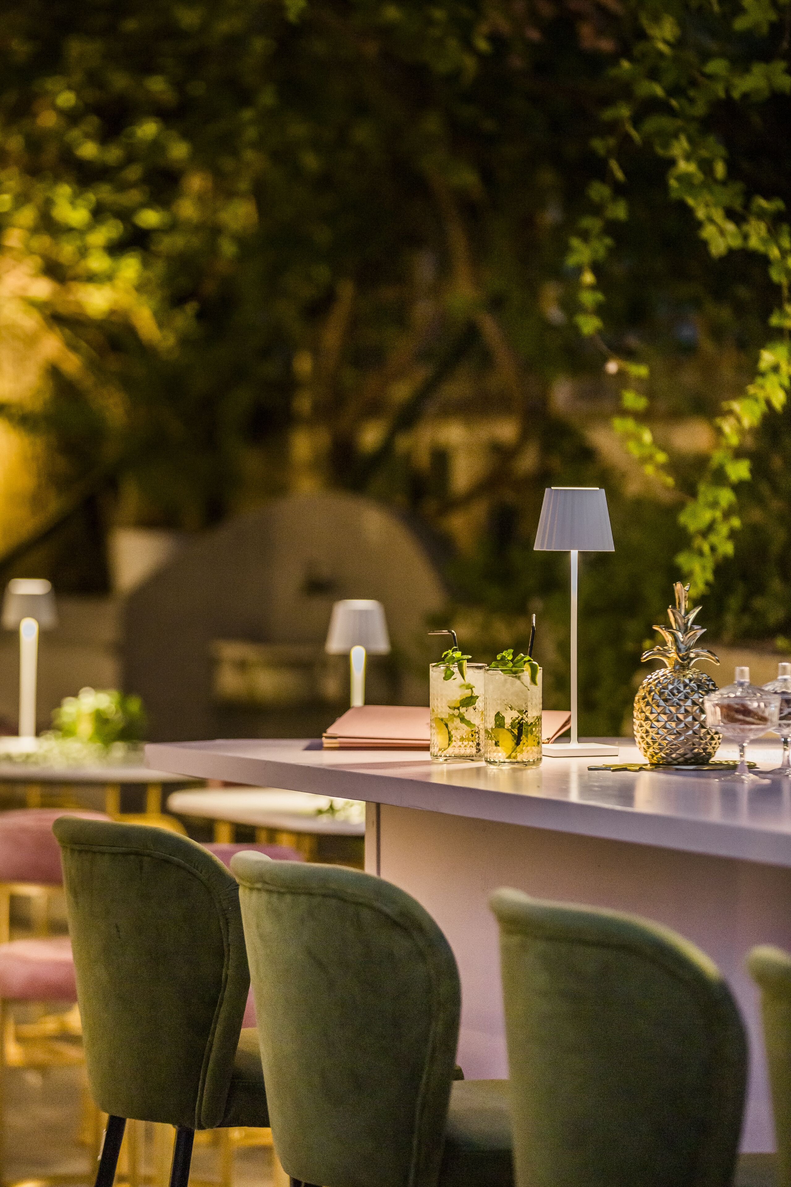 An outdoor bar area with green chairs, a table with drinks, and a lamp.